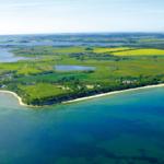 Aerial view of coastal landscape with green fields, lakes, and sandy beach.