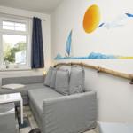 Wohnzimmer mit grauem Sofa, Wandmalerei und Fenster mit Vorhängen.