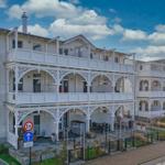 Weiße Ferienwohnung mit Balkonen und Gartenbereich unter blauem Himmel.