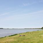 Mensch liegt auf Gras am Ufer eines Sees unter blauem Himmel.