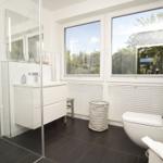 Badezimmer mit Dusche, Waschbecken und Toilette. Große Fenster mit Blick auf Grün.