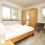 Schlafzimmer mit Holzbett, Kleiderschrank und Fenstern mit Blick auf Garten.