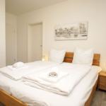 Schlafzimmer mit Doppelbett, Holzgestell und Nachttisch mit Lampe.