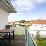 Terrasse mit Tisch und Stühlen, Blick auf Wohnhäuser und Grünflächen.