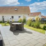 Terrasse mit Sitzgruppe, Garten und Nachbarhäuser unter blauem Himmel.
