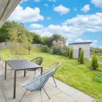 Terrasse mit Tisch und Stühlen, Grünfläche und kleinem Gartenhaus im Hintergrund.