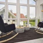 Zwei schwarze Schaukelstühle stehen auf einem dunklen Teppich vor großen Fenstern.