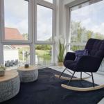 Ein Raum mit großem Fenster, Schaukelstuhl und zwei runden Tischen.