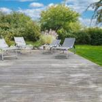 Vier Liegestühle auf einer Holzterrasse im Garten mit Gras und Bäumen.