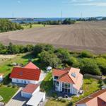 Haus mit rotem Dach und Garten, umgeben von Feldern und einem See.