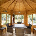 Holzvertäfelte Terrasse mit Esstisch und Stühlen. Große Fenster bieten Blick auf Garten.