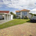 Modernes Haus mit Garage und gepflastertem Vorplatz. Grünfläche und geparkte Autos.