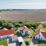 Haus mit rotem Dach und Garten, umgeben von Feldern und Bäumen.