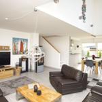 Wohn- und Essbereich mit Sofa, TV und Tisch. Durchgang zur Küche und Terrasse.