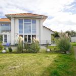 Moderne Villa mit Terrasse und Garten. Parkplatz und Pflanzen sind vorhanden.