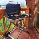 Grill steht auf Terrasse neben Hauswand mit Blick auf Garten.