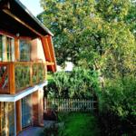 Haus mit Balkon, Garten und Bäumen. Holzgeländer und Ziegelwand sichtbar.