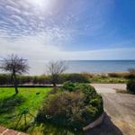 Meerfront mit Grünfläche und Parkplatz. Blick auf die Küste unter blauem Himmel.