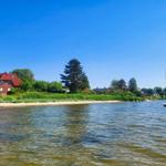 Haus am Wasser mit Segelbooten und grüner Umgebung.