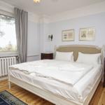 Schlafzimmer mit Doppelbett, Holzboden und Fensterblick auf Bäume.