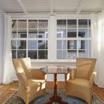 Zwei Stühle und ein Tisch stehen vor großen Fenstern mit weißen Vorhängen.