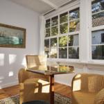 Zwei Stühle und ein Tisch stehen vor einem großen Fenster. An der Wand hängt ein Bild mit Schiffen.