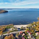 Aerial view of a coastal village with houses, beach, and large water body surrounded by autumn-colored forests.