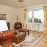 Wohnzimmer mit Ledersofa, Holzboden und Fenster mit gelben Vorhängen.