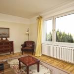 Raum mit braunem Ledersessel, Holzboden und Fenster mit goldfarbenen Vorhängen.