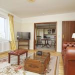 Wohnzimmer mit Ledersofa, Fernseher und Blick auf die Küche.