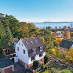 Wohnhaus mit Blick auf See und Turm, umgeben von Herbstbäumen.