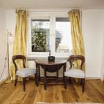 Zimmer mit Holzboden, Tisch, zwei Stühle und Fenster mit Vorhängen.