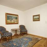 Zimmer mit zwei Stühlen, Tisch und Teppich. Wandbilder und Holzboden.