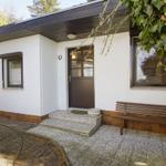 Eingangsbereich mit brauner Tür, Bank und Pflanzen.