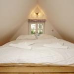 Doppelbett unter Dachschräge mit Fenster und Wandlampe.