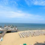 Strand mit Strandkörben, Pier und Meer unter blauem Himmel.