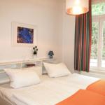 Zimmer mit Doppelbett, Fenster, Vorhängen und Deckenleuchte.