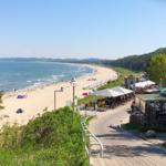 Strandpromenade mit Strand, Bäumen und Terrassenbereich.