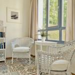 Zwei weiße Rattan-Stühle stehen vor einem großen Fenster mit Blick auf Grün.