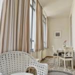 Raum mit Sitzgelegenheit, Esstisch und Fenstern mit Vorhängen.