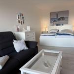 Schlafzimmer mit Sofa, Bett und Tisch. Wandbild zeigt Leuchtturm.