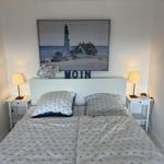 Schlafzimmer mit Bett, Nachttischen und Wandbild mit Leuchtturm.