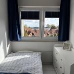 Ein Schlafzimmer mit Blick auf Dächer und See. Bett, Schrank und Fenster sind sichtbar.