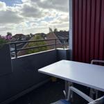 Terrasse mit Tisch und Stühlen, Blick auf Dächer und Himmel.