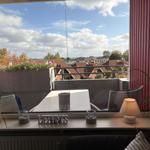 Balkon mit Tisch, Stühlen und Blick auf Dächer und Meer.