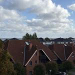 Rotes Dach mit Schornsteinen und Blick auf Meer und Bäume.