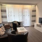 Wohnzimmer mit Sofa, Sesseln, TV und Fenster mit Vorhängen.