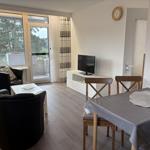 Wohn- und Essbereich mit Fernseher, Tisch und Stühlen. Balkon mit Blick auf Bäume.