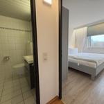 Schlafzimmer mit Bett und Fenster. Nebenraum ist Badezimmer mit Dusche.