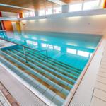 Innenpool mit Treppe und Holzdecke. Wandverkleidung aus weißen und orangefarbenen Fliesen.